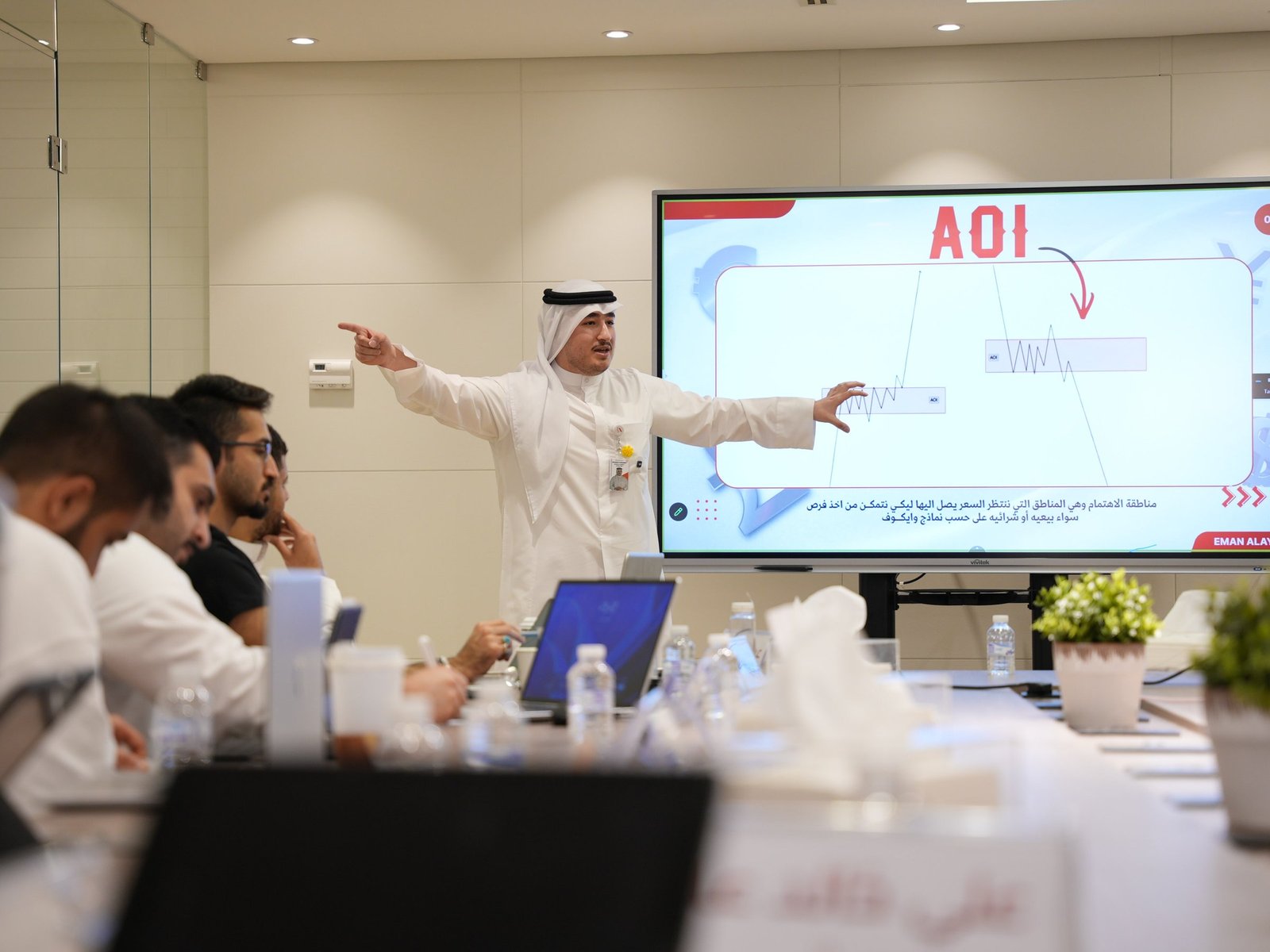 A trainer explaining an area of interest on a large screen to a group of clients in the Eman Alayyaf trading hall