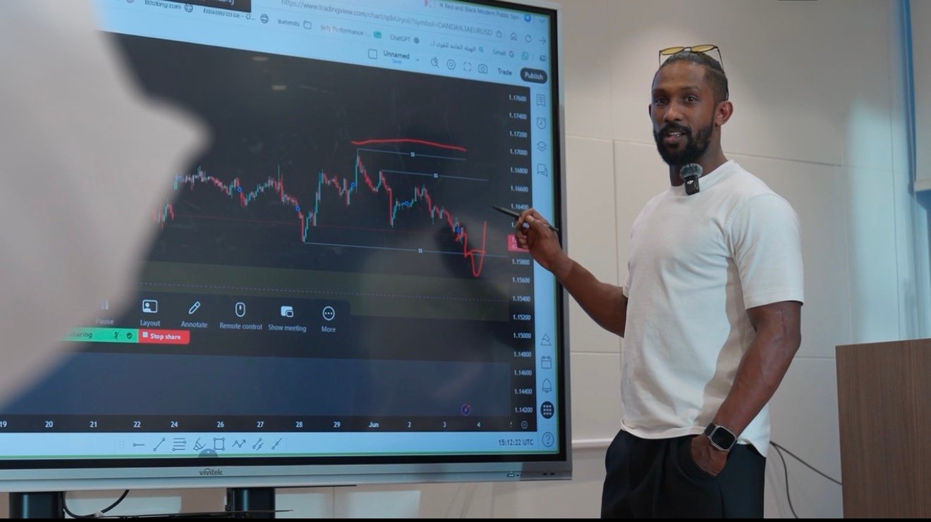 A trainer pointing at a live forex chart on the big screen during a workshop